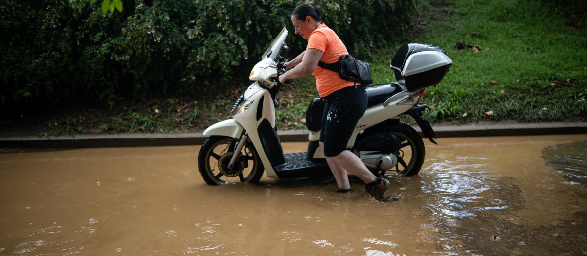 Una mujer empujando su moto en un barrio de Barcelona debido a las inundaciones
