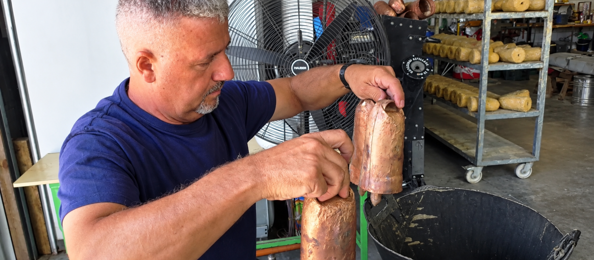 Juan Chamizo sostiene dos cencerros fabricados artesanalmente en su taller familiar