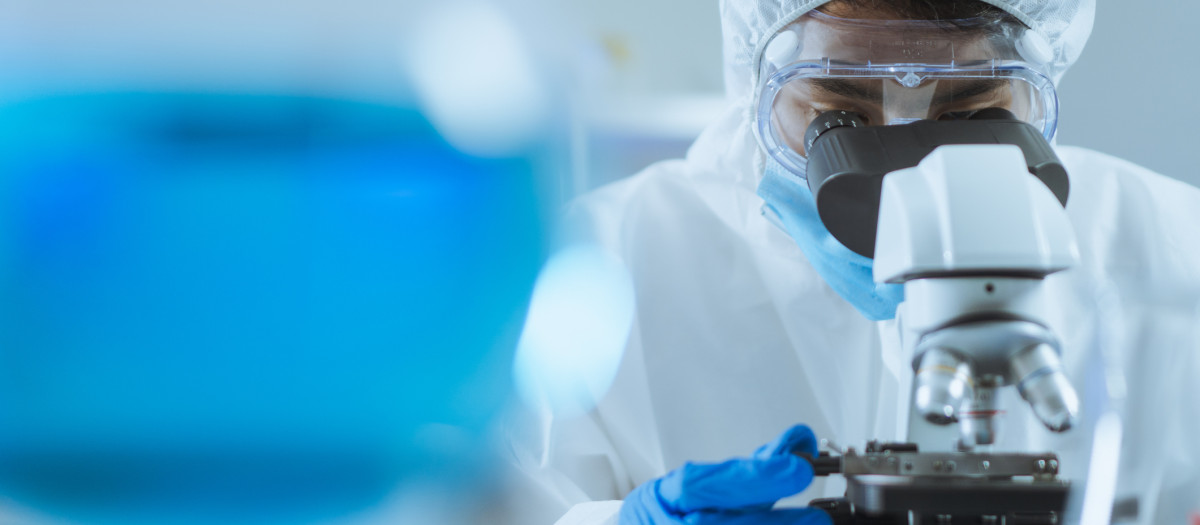 Imagen de archivo de un científico mirando un microscopio vestido con un EPI