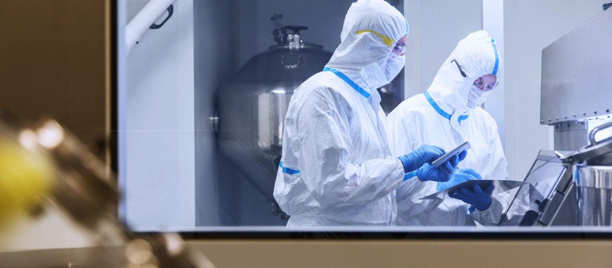 Científicos con trajes limpios usando tabletas digitales en experimentos en laboratorio