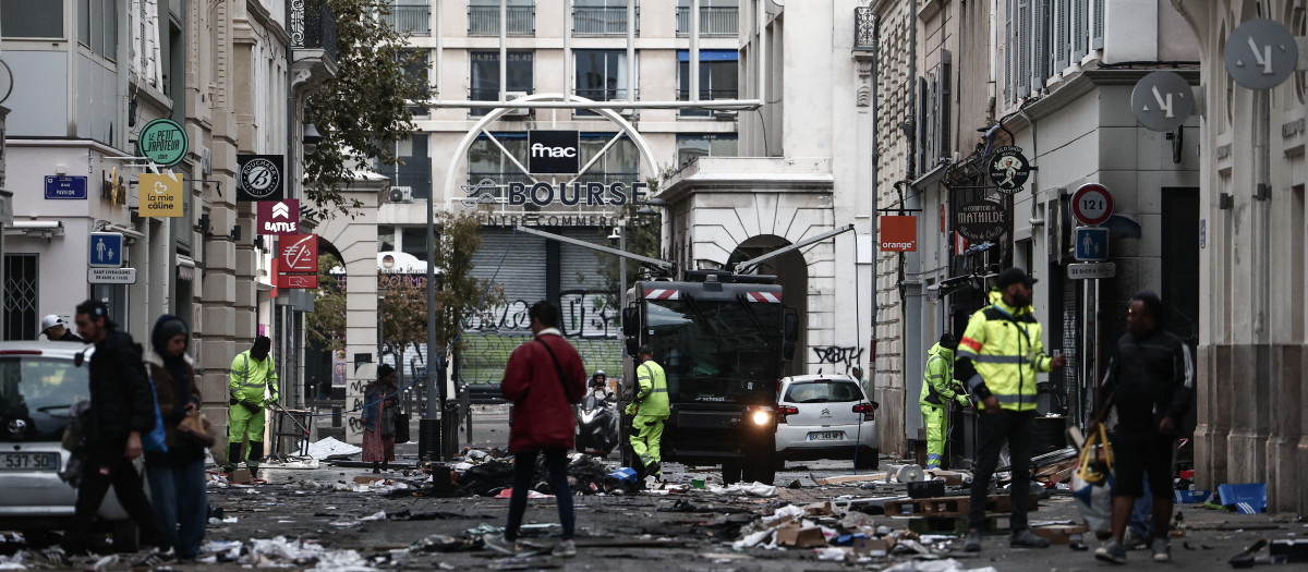 Trabajadores de la municipalidad de Marsella limpian los destrozos en una calle comercial