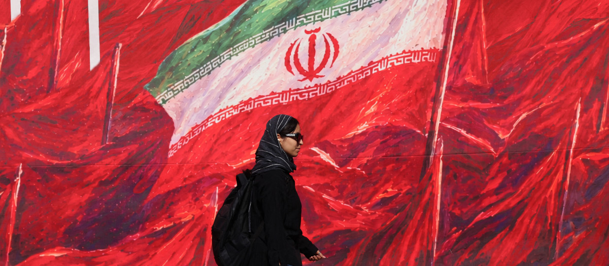 Una mujer pasa junto a un mural con la bandera nacional iraní en Teherán