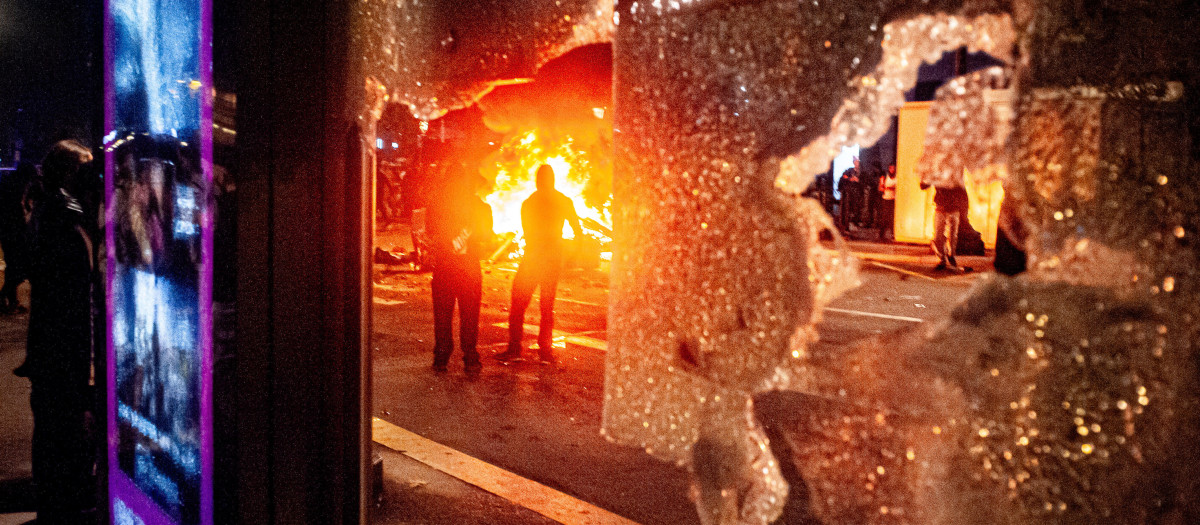Imagen de una barricada en llamas a través de los cristales rotos de una parada de autobús en medio de los disturbios en el centro de Barcelona