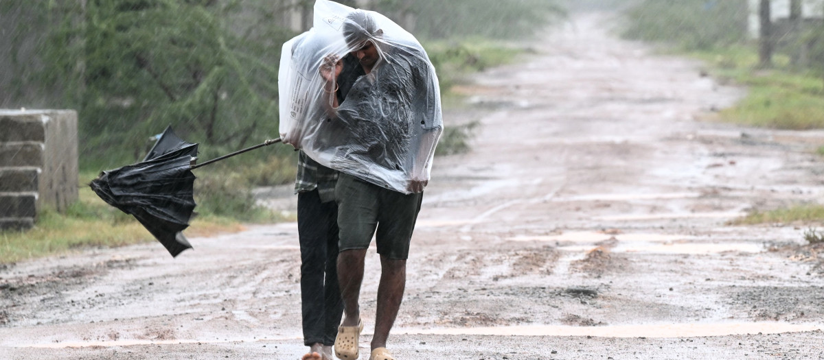 Unos hombres utilizan una lámina de plástico para cubrirse durante la lluvia en Kakinada