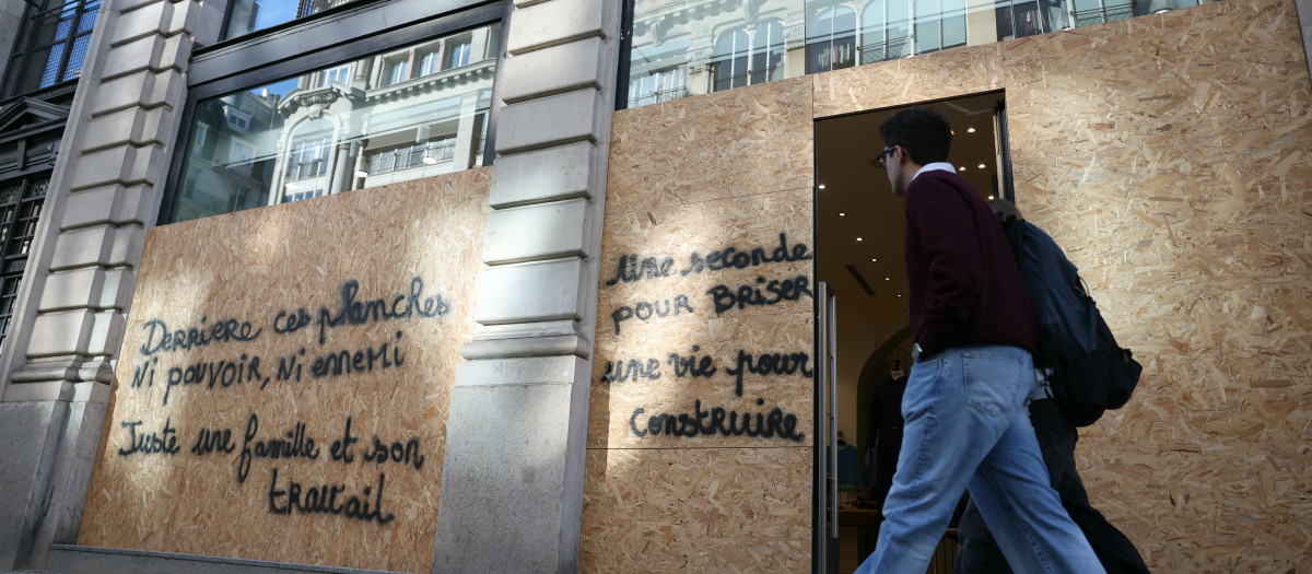 Los peatones pasan junto a una tienda protegida por tablones de madera en los que está escrito (I) "Detrás de estos tablones, ni poder, ni enemigo", solo una familia y su trabajo"