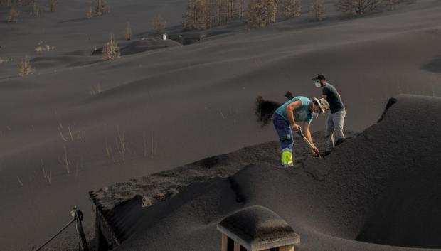 Personas limpiando el tejado de las casas cubierto por la ceniza del volcán de La Palma en Las Manchas