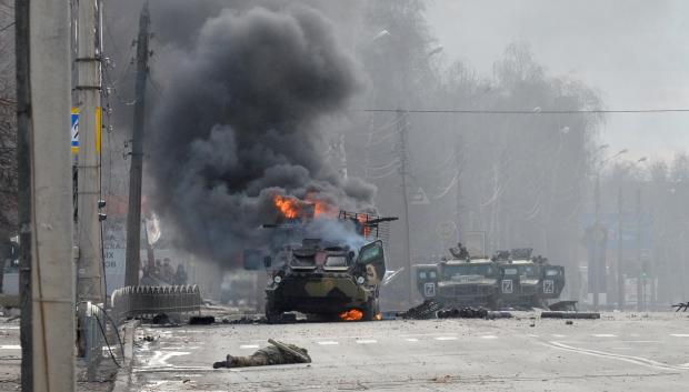 Un vehículo blindado ruso ardiendo junto al cuerpo de un soldado