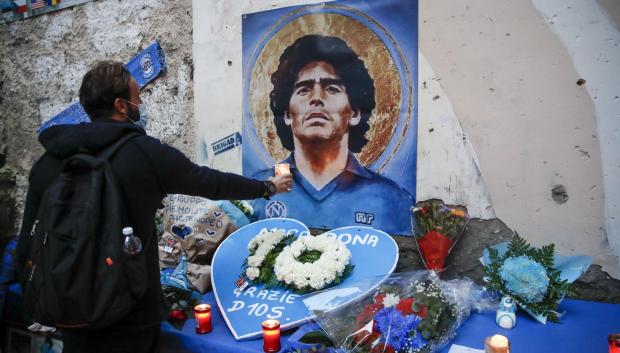 Un hombre coloca una vela encendida en el altar improvisado de Maradona en Nápoles