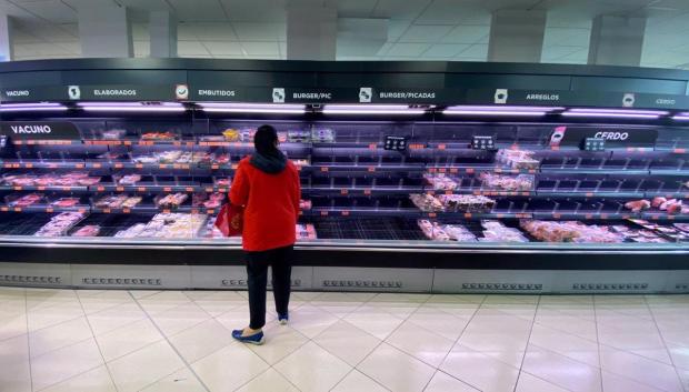 Una mujer observa los alimentos que quedan en los refrigeradores de carne de un supermercado un día marcado por colas de gente deseosas de hacer acopio de alimentos