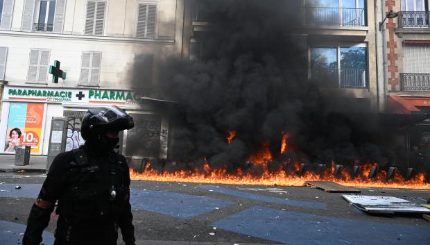 Un agente de Policía junto a una estación de bicicletas públicas ardiendo en París