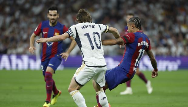 El centrocampista croata del Real Madrid Luka Modrić (c) disputa un balón con el delantero brasileño del FC Barcelona Raphinha