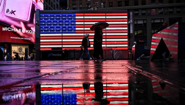 Un grupo de personas pasa junto a una bandera estadounidense en Times Square