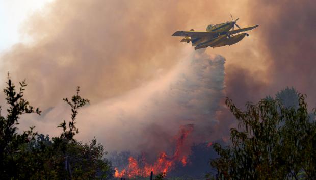 An Air Tractor AT-802F Fire Boss aircraft dumps water over a wildfire burning near San Martin de Valdeiglesias, about 70km west of Madrid, on July 26, 2026. Spanish firefighters today battled a new front of fires near the coastal city of Valencia, where at least 15,000 people were evacuated. In the western Madrid region, two separate wildfires merged on July 24 into a massive blaze that nearly joined another fire in neighboring Castile and Leon. The flames have already burned 25,000 hectares across Madrid and neighboring Avila province, forcing more than 60,000 people (a downwardly revised figure) to flee their homes, according to authorities, who labeled the fire the "worst in history" for the Madrid region. (Photo by Cesar MANSO / AFP)