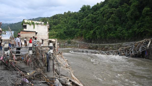 Unas personas permanecen cerca de un puente colapsado tras unas inundaciones repentinas en Devighat, en el distrito nepalí de Nuwakot