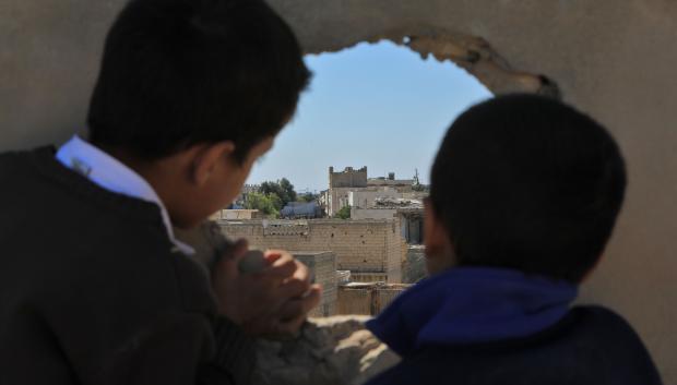 Niños sirios miran a través de un agujero en una frontera que separa el régimen y el territorio controlado por los rebeldes en la ciudad norteña de Tadif