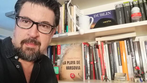 Mario Flores frente a su librería, con la novela 'La playa de Varsovia' en primer plano