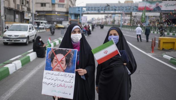 Dos mujeres iraníes llevan una bandera nacional y una pancarta anti Masih Alinejad durante una marcha en conmemoración de la revolución islámica