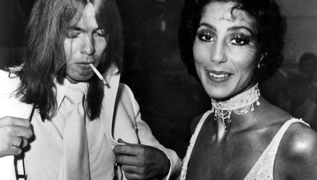 GREGG ALLMAN and CHER, c. mid-1970s 
1970s 1970s fashion 1960s portraits Allman,gregg Beaded dress Candid Chelbd Cher Choker Cigarette Couple Flapper Long hair Lovers Men's fashion Necklace Rock and roll Smoking book Women's fashion