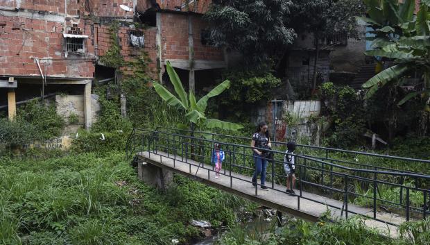 A woman and her kids cross a bridge over the Catuche stream, at the Catuche neighbourhood in Caracas, Venezuela, on November 26, 2022. - The Catuche neighbourhood is part of a socio-spatial urban plan "El sueño de Catuche" (Catuche's dream), which began in 2018 within the framework of an inter-institutional cooperation and research programme sponsored by the French embassy in Venezuela and agreements between Venezuelan universities. (Photo by Miguel ZAMBRANO / AFP)