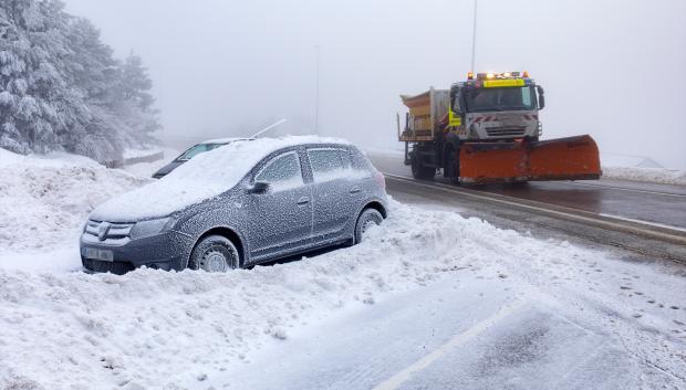 Un coche cubierto de nieve y una máquina quitanieves en Navacerrada