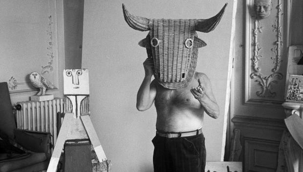 Pablo Picasso with a wicker bull mask originally intended for bullfighters' training, he becomes a living Minotaur. Beside him is a sculpture made of scrap wood with the features painted on it. La Californie, Cannes 1959.