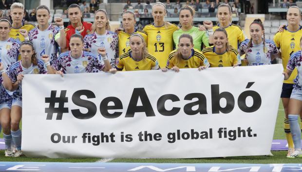 Las jugadoras de ambas equipos posan con una pancarta que reza ¡Se acabó, nuestra lucha es global'