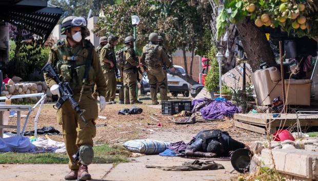 Israeli soldiers stand near the body of a Palestinian militant in Kfar Aza, in the south of Israel, bordering Gaza Strip on October 10, 2023. Israel pounded Hamas targets in Gaza on October 10 and said the bodies of 1,500 Islamist militants were found in southern towns recaptured by the army in gruelling battles near the Palestinian enclave. (Photo by Thomas COEX / AFP)