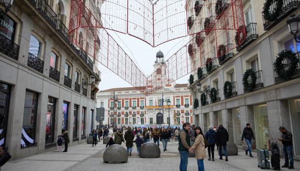 Varias personas en una calle comercial frente a la remodelada y peatonalizada Puerta del Sol