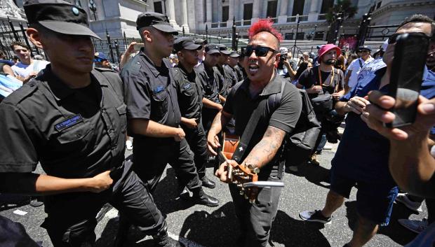 Un hombre toca la guitarra junto a policías que resguardan las instalaciones del Congreso argentino durante un paro nacional contra el gobierno de Javier Milei en Buenos Aires