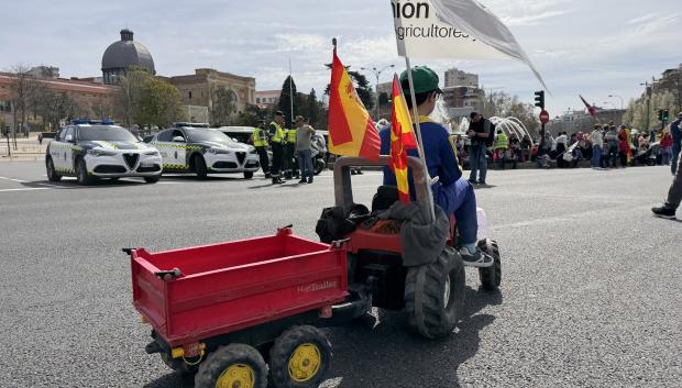 Un niño montado en un tractor de juguete con banderas de España asiste a la protesta