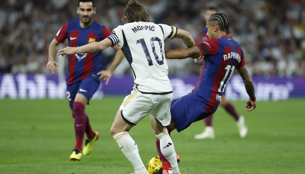 El centrocampista croata del Real Madrid Luka Modrić (c) disputa un balón con el delantero brasileño del FC Barcelona Raphinha
