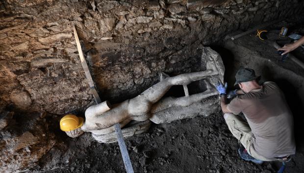 Un arqueólogo trabaja junto a la antigua estatua recién descubierta durante las excavaciones en la antigua ciudad de Heraclea Sintika