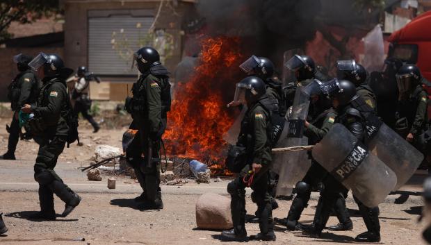 Integrantes de la Policía Boliviana caminan por una vía bloqueada y con llantas quemándose por simpatizantes del expresidente de Bolivia, Evo Morales