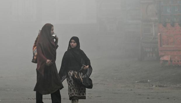 Dos mujeres caminan por una carretera envuelta en una espesa niebla tóxica en Lahore