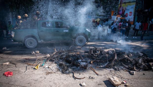 Integrantes de la Policía de Haití pasan frente a los restos de un pandillero incinerado