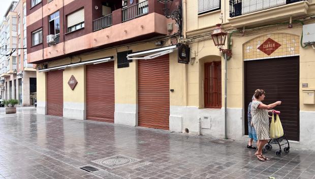 Imagen de dos mujeres paseando ante la persiana cerrada de la Taberna El Carrer de Campanar en el mes de septiembre.