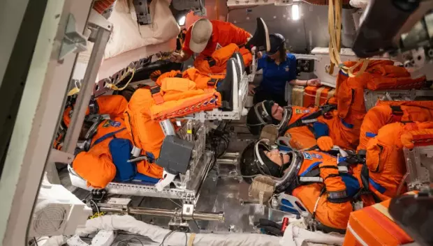 La tripulación de Artemis II se coloca sus trajes espaciales del sistema de supervivencia de la tripulación Orion para la salida de emergencia posterior al aterrizaje dentro de la maqueta Orion en las instalaciones de maquetas de vehículos espaciales de Johnson