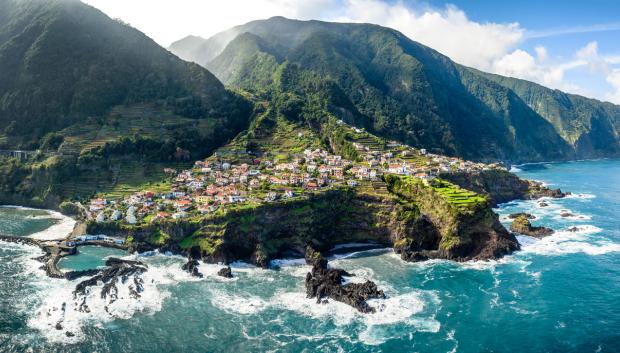 Seixal village nestled on Madeira's dramatic coastline, revealing whitewashed houses, terraced landscapes cascading toward sparkling Atlantic waters under golden sunlight
