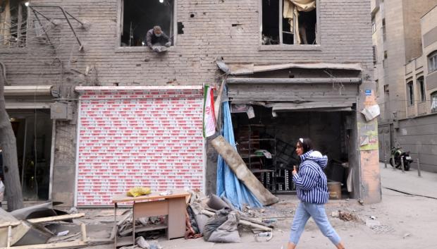 Una mujer camina junto a edificios dañados tras un ataque militar a la capital iraní