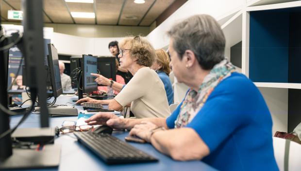Personas mayores siguiendo las instrucciones de una docente en sus ordenadores