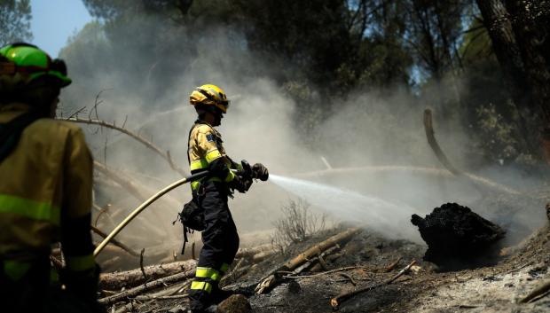 Bomberos rocían agua sobre el terreno para evitar que el fuego se reavive tras lograrse controlar un incendio cerca de La Adrada