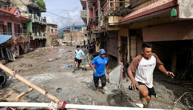 Residentes locales caminan junto a casas sumergidas en lodo tras las inundaciones repentinas