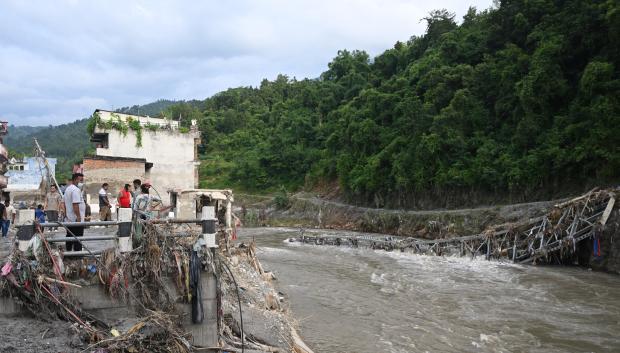 Unas personas permanecen cerca de un puente colapsado tras unas inundaciones repentinas en Devighat, en el distrito nepalí de Nuwakot