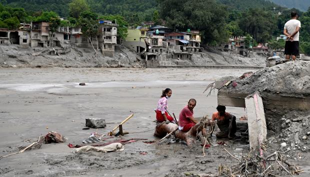 Unos residentes se sientan junto a los escombros mientras recuperan sus pertenencias tras unas inundaciones repentinas en Devighat
