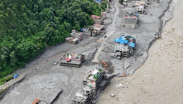 Una vista aérea muestra un torrente de agua fangosa que avanza con fuerza junto a las viviendas y a través del río Trishuli