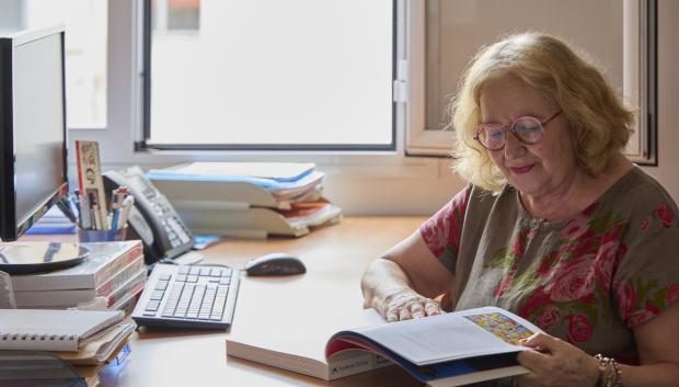 Persona mayor en un escritorio ojeando un libro