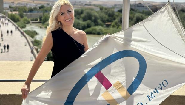 Lourdes Morales en la Puerta del Puente junto a la bandera de las ciudades patrimonio
