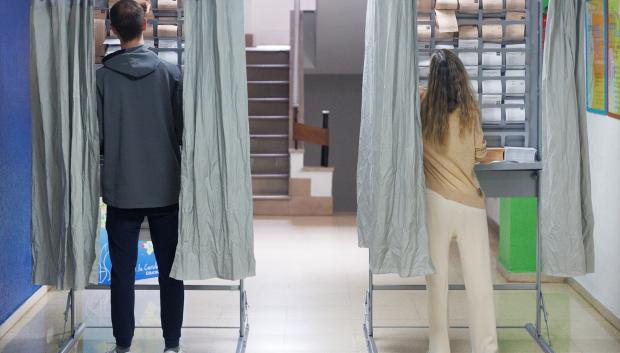 Dos personas ejercen su derecho a voto en una cabina en un colegio electoral