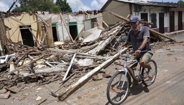Un hombre pasa en bicicleta frente a escombros de casas dañadas por el terremoto
