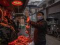 Un hombre con una mascarilla escoge un pollo en el mercado callejero de Wuhan
